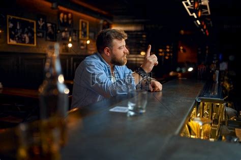 大胡子男人坐在酒吧的柜台前。都市夜景人物活动高清摄影大图-千库网