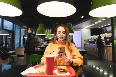 女孩用智能手机在快餐店吃饭高清图片下载-正版图片505724653-摄图网