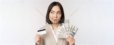体贴的女商人、韩国企业女性展示信用卡和现金、手中的美元、站在白色背景下思考高清摄影大图-千库网