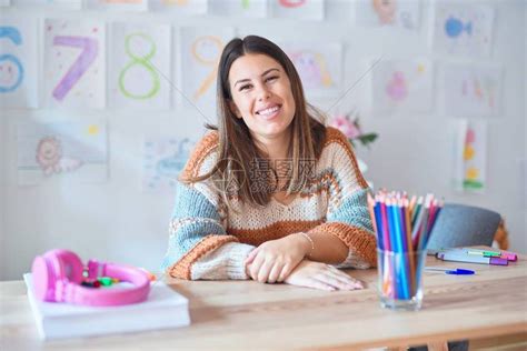 年轻美丽的女教师穿着毛衣和眼镜坐在幼儿园的办公桌上高清图片下载-正版图片504374519-摄图网