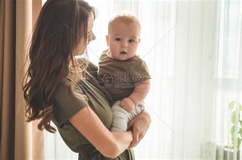 一个男婴的家庭肖像与靠近窗户的母亲妈抱着和亲吻她的孩子高清图片下载-正版图片503365537-摄图网