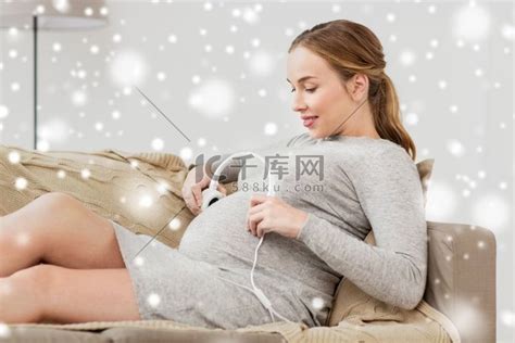 怀孕、音乐和人的概念-快乐的孕妇在雪地上拿着耳机在家里的肚子上。高清摄影大图-千库网