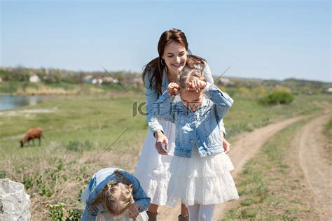 母亲带着她的双胞胎女儿沿着奶牛附近村庄的土路行走。高清摄影大图-千库网