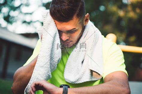 汗流浃背的健康男人在锻炼后用毛巾擦拭自己，同时看着手表高清摄影大图-千库网