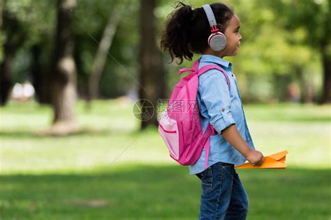 在公园走动时持纸机的耳机中可爱的非洲女学高清图片下载-正版图片503356782-摄图网