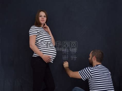 怀孕的年轻夫妇记下了怀孕周，并用粉笔在黑板上写下了它们。海军条纹短袖高清摄影大图-千库网