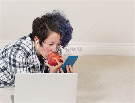 女孩一边吃苹果看手机前面有电脑一边躺着听家里的音乐高清图片下载-正版图片304109419-摄图网