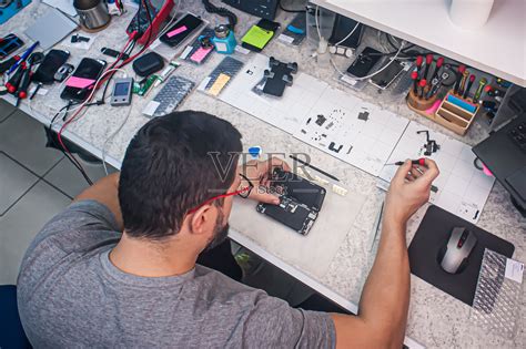 在电子修理厂，修理工用螺丝刀拆卸智能手机照片摄影图片_ID:433746446-Veer图库