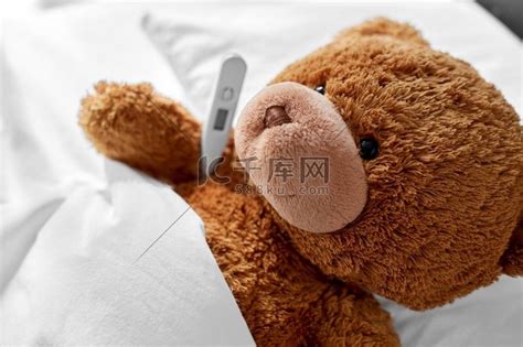 医学、医疗保健和童年概念-生病的泰迪熊玩具头，床上有温度计。高清摄影大图-千库网
