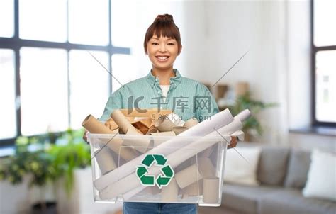 回收、废物分类和可持续性概念-快乐微笑的亚洲年轻女性在家庭背景下拿着塑料盒里的纸垃圾。高清摄影大图-千库网