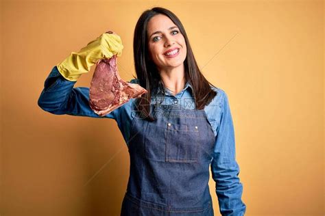 身着围裙的年轻屠夫女人拿着生牛排高清图片下载-正版图片504238041-摄图网