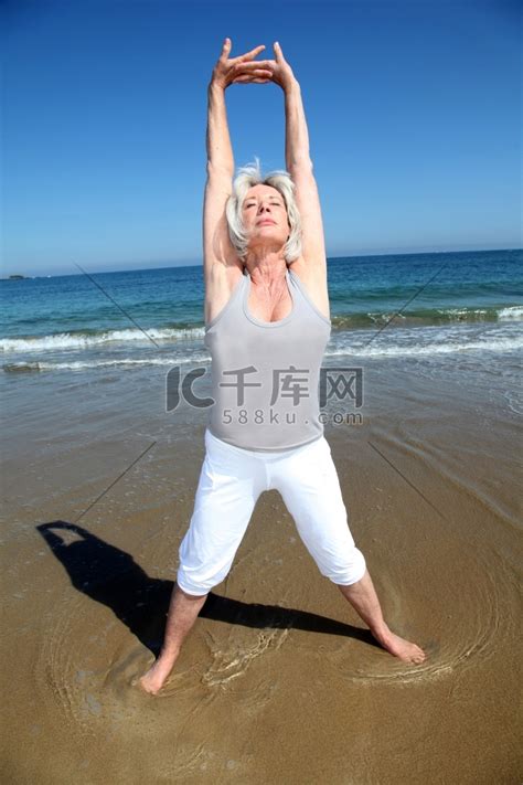 一位老年妇女在海滩上做伸展运动瑜珈瑜伽高清摄影大图-千库网