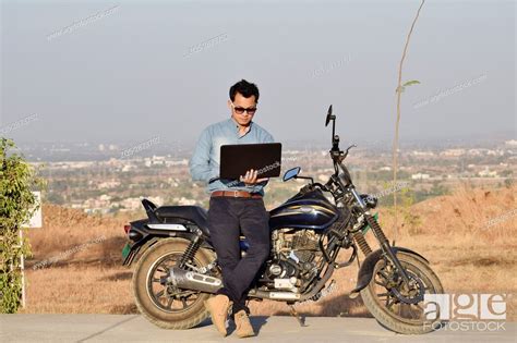 Young man sitting on bike working on laptop near mountain, Pune ...