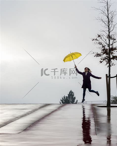 下雨天，女人拿着一把黄色的雨伞在地平线上跳跃。高清摄影大图-千库网