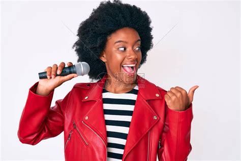 年轻的非裔美国女人唱着歌用麦克风指着拇指向侧面笑高清图片下载-正版图片503861547-摄图网