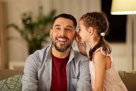 家庭、父亲身份、休闲和人的概念-快乐的女儿晚上在家里向父亲耳语秘密。高清摄影大图-千库网