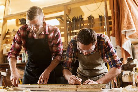 职业、木工、木工和人的概念-两个快乐的木匠在车间用电钻和木板。高清摄影大图-千库网