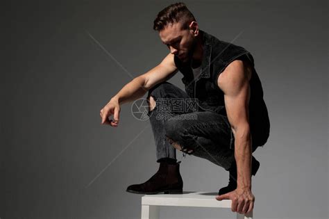 灰色工作室背景中穿着黑色牛仔裤背心的帅哥蹲下并高清图片下载-正版图片503838840-摄图网