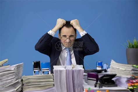 感觉疲倦和劳累过度的商人在办公桌上满是文书工作发票和大量文件和文件时撕扯着头发过度工作的概念疲劳高清图片下载-正版图片503933072-摄图网