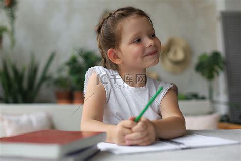 小女孩坐在书桌前，在笔记本上写字，在家做练习，小孩子手写准备作业。高清摄影大图-千库网