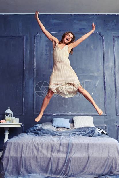 一个有吸引力的年轻女子在床上精力充沛地跳跃的低角度穿着睡衣的女人非常兴奋地跳上床高清图片下载-正版图片502541408-摄图网