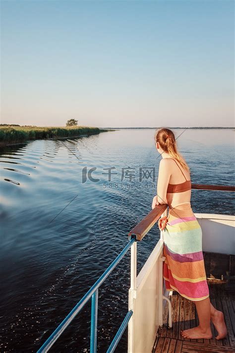 一个美丽的年轻女孩站在船头，看着宁静的傍晚日落。高清摄影大图-千库网