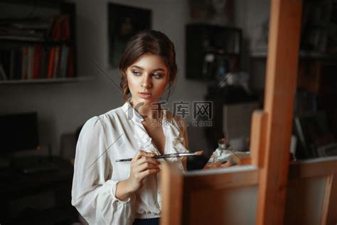 在画室里，有调色板和画笔的体贴的女画家站在画架上。高清摄影大图-千库网