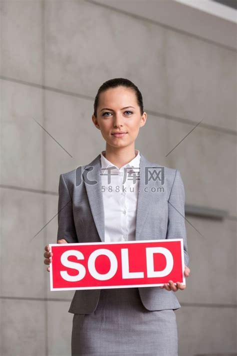 自信的年轻女售货员在公寓里靠墙站立时手持售出标语牌的画像高清摄影大图-千库网