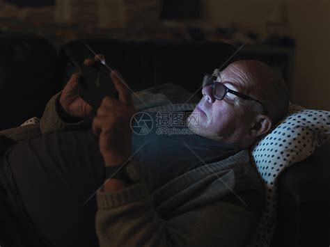 成熟的男人，晚上躺在沙发上，用智能手机，脸上有灯光高清图片下载-正版图片501438014-摄图网