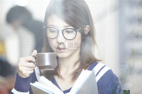 年轻女子拿着一杯咖啡，望着窗外。她在咖啡馆喝咖啡高清摄影大图-千库网