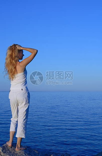 画像中一名美丽的年轻游客(女孩)，身穿白色连衣裙，相貌姣好，背着双肩包，戴着草帽，走在岩石、大海和山峦之间。视频素材_ID ...