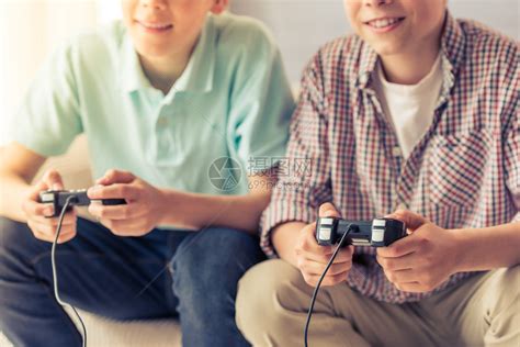 两名有吸引力的少年男孩在家里坐在沙发上玩游戏控制台和笑着微高清图片下载-正版图片504941675-摄图网