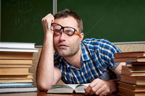 一位戴着眼镜的疲惫不堪衣冠不整衣冠不整的学生正睡在一张桌子旁高清图片下载-正版图片505627472-摄图网