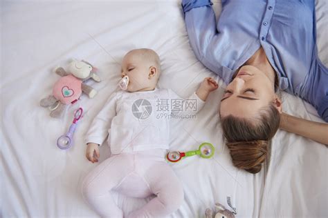 母亲在家中坐在床上时用奶嘴抱着婴高清图片下载-正版图片503474028-摄图网