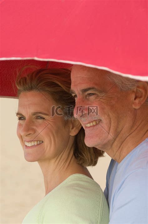 一对情侣在海滩遮阳伞下避难高清摄影大图-千库网