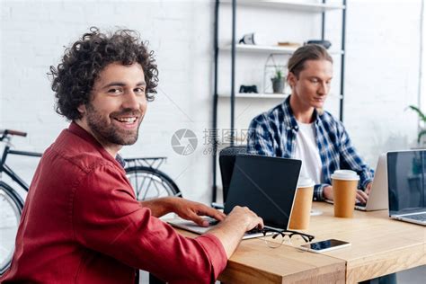 青年男子在与办公室同事一起工作时使用带空白屏幕的笔记本电脑高清图片下载-正版图片502577611-摄图网