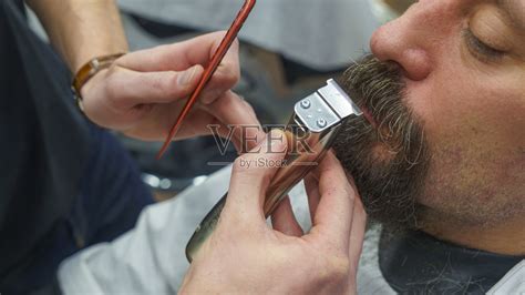 理发师在理发店里用剃须机修剪胡子。弄头发的过程。发型的概念。照片摄影图片_ID:377720256-Veer图库