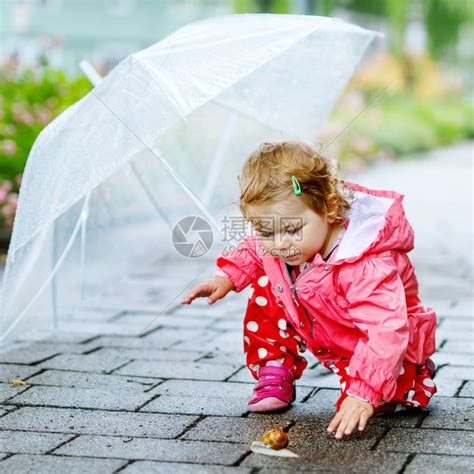 可爱的女婴在散步时发现蜗牛美丽的卷曲蹒跚学步的孩子在下雨天玩得开心带着大伞高清图片下载-正版图片504254920-摄图网
