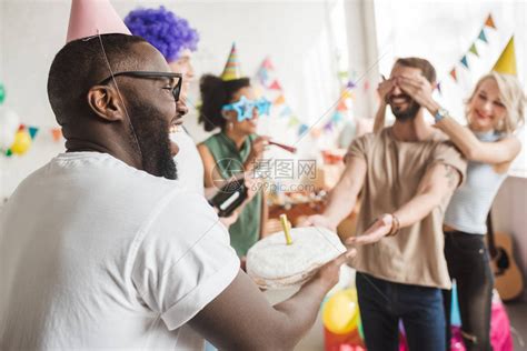 快乐的朋友遮着年轻男人的眼睛用生日蛋糕向他问好高清图片下载-正版图片502515636-摄图网