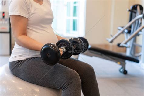 活跃的孕妇在瑜伽室的健身中心锻炼年轻的准妈抱着婴儿在怀孕的肚子里产前护理和高清图片下载-正版图片504512025-摄图网