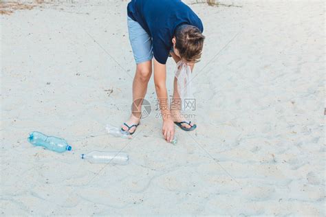 戴着手套的蓝色T恤的男孩将垃圾和塑料瓶收集到海滩上的包裹中高清图片下载-正版图片506504702-摄图网