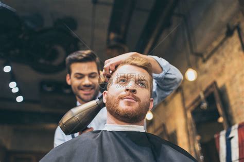年轻的理发师在理发店用吹风机吹干顾客的头发高清图片下载-正版图片502662197-摄图网
