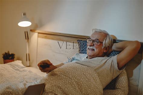 快乐成熟的男人晚上躺在床上看电视。照片摄影图片_ID:352696750-Veer图库