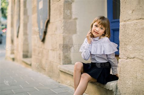 户外时尚街头的城市小白脸女孩肖像。快乐的小女孩坐在古老的欧洲城市老建筑墙附近，蓝色的门在背景上