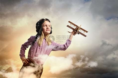 戴着飞行员帽子的小女孩飞行员头盔中的小女孩云背景下玩玩具飞机的形象高清图片下载-正版图片300323523-摄图网