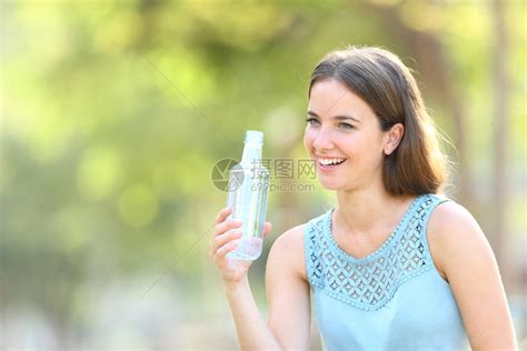 带着塑料水瓶的快乐女人在一个绿色背景的公园里四处看高清图片下载-正版图片305354507-摄图网