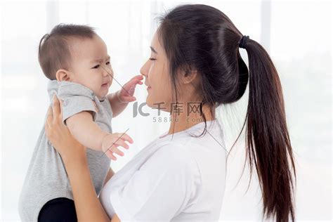 年轻的亚洲母亲在家里的卧室里抱着小女婴，妈妈带着孩子和照顾孩子，女人和孩子无忧无虑，蹒跚学步的孩子和父母，情感和表达，家庭观念。高清摄影大图-千库网