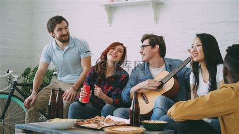 快乐的年轻朋友在合租公寓举办派对，一起唱歌，而他们的朋友在家里弹吉他高清摄影大图-千库网
