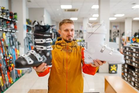 男子在体育用品商店展示白色和黑色的滑雪靴或单板滑雪靴。高清摄影大图-千库网