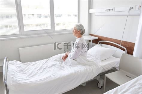 医学、医疗保健和人的概念-孤独的老年妇女坐在医院病房的床上。高清摄影大图-千库网